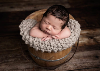 Baby boy asleep in bucket on wooden floor photographed by Newborn Photographer Olney